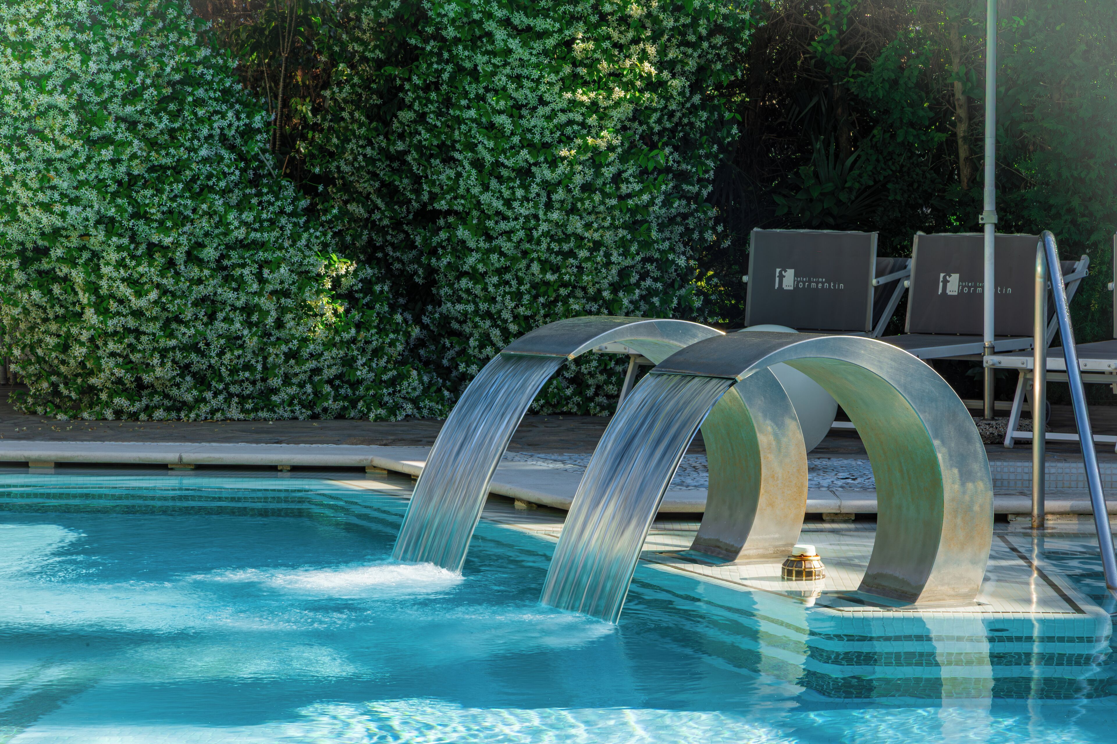 Une piscine agrémentée d’une cascade et de chaises longues.