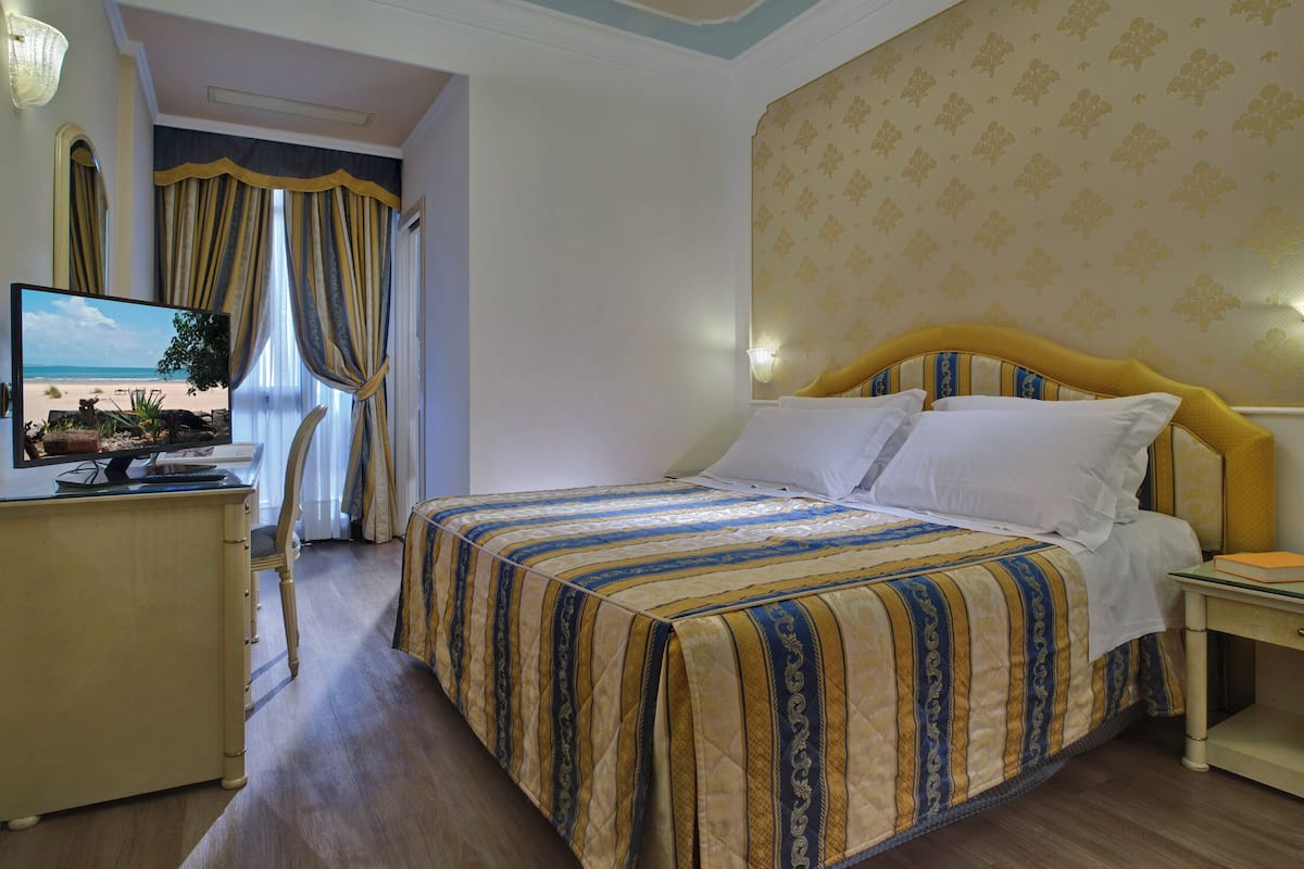 A hotel room with a bed, a desk, a chair, and a television.