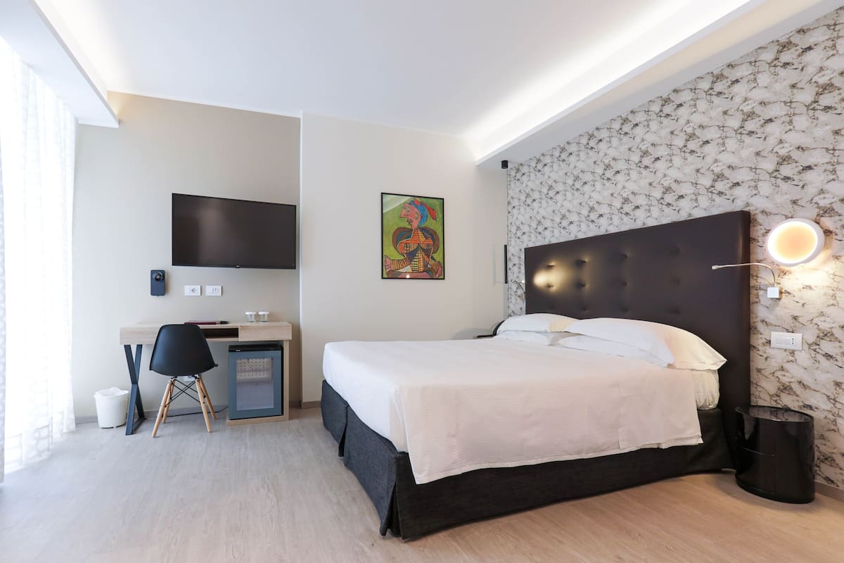 A modern hotel room with a bed, desk, and TV.
