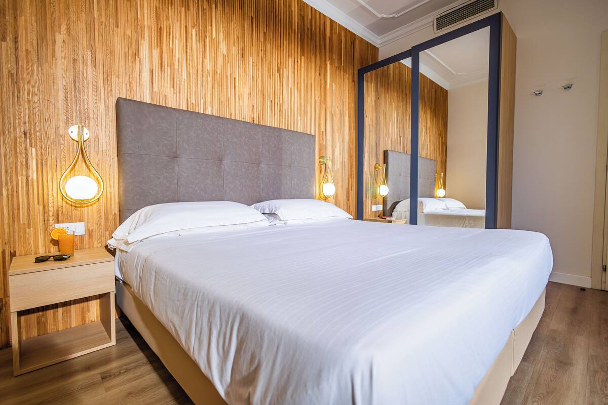 A neatly made bed with white linens, a wooden headboard, and bedside lamps.