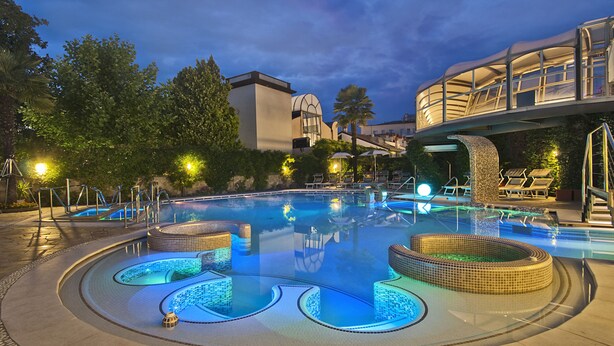 A swimming pool with a unique design, surrounded by lounge chairs and a covered walkway. - Formentin Terme (Abano Terme)