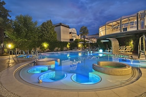A swimming pool with a unique design, surrounded by lounge chairs and a covered walkway. - Formentin Terme (Abano Terme)