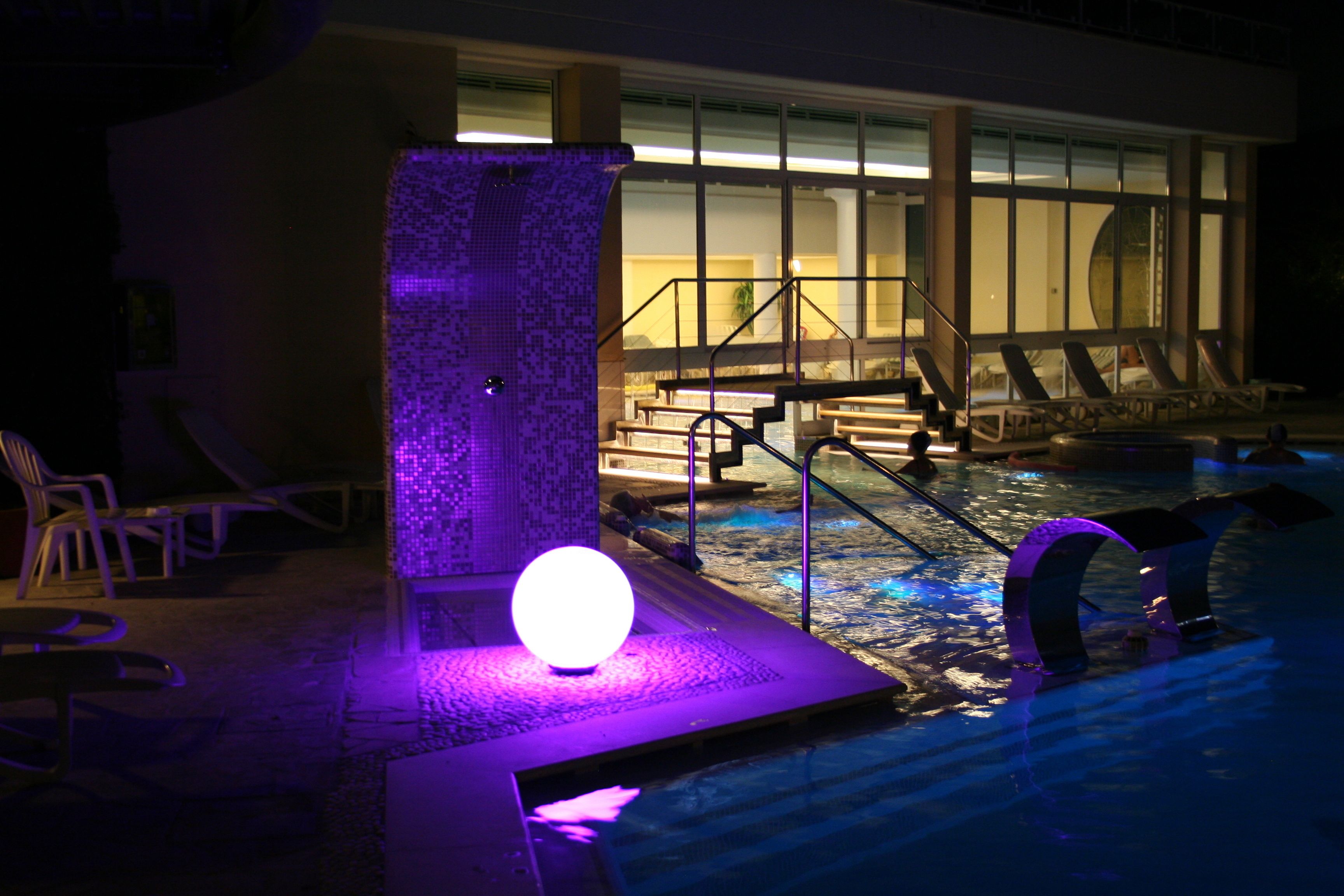 Un espace piscine agrémenté d’un luminaire sphérique, de chaises longues et d’un escalier menant à une terrasse.