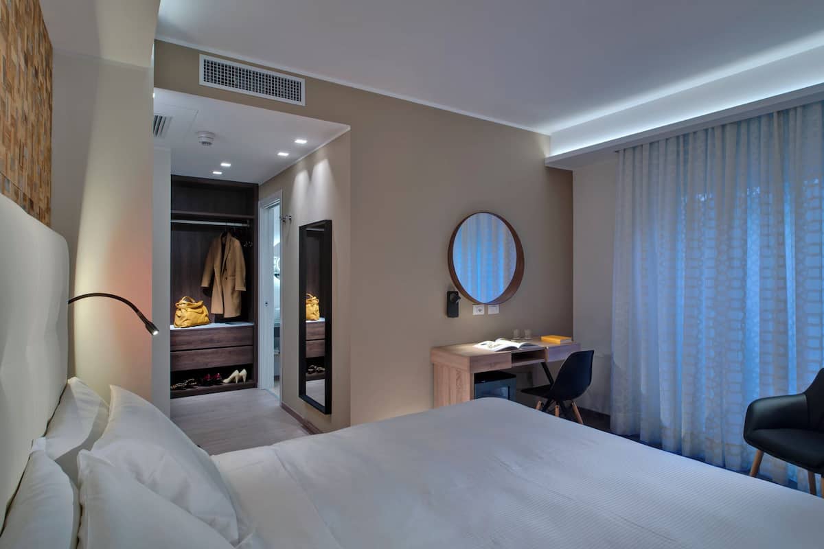 A hotel room with a large bed, a desk with a chair, a wardrobe, and a mirror.