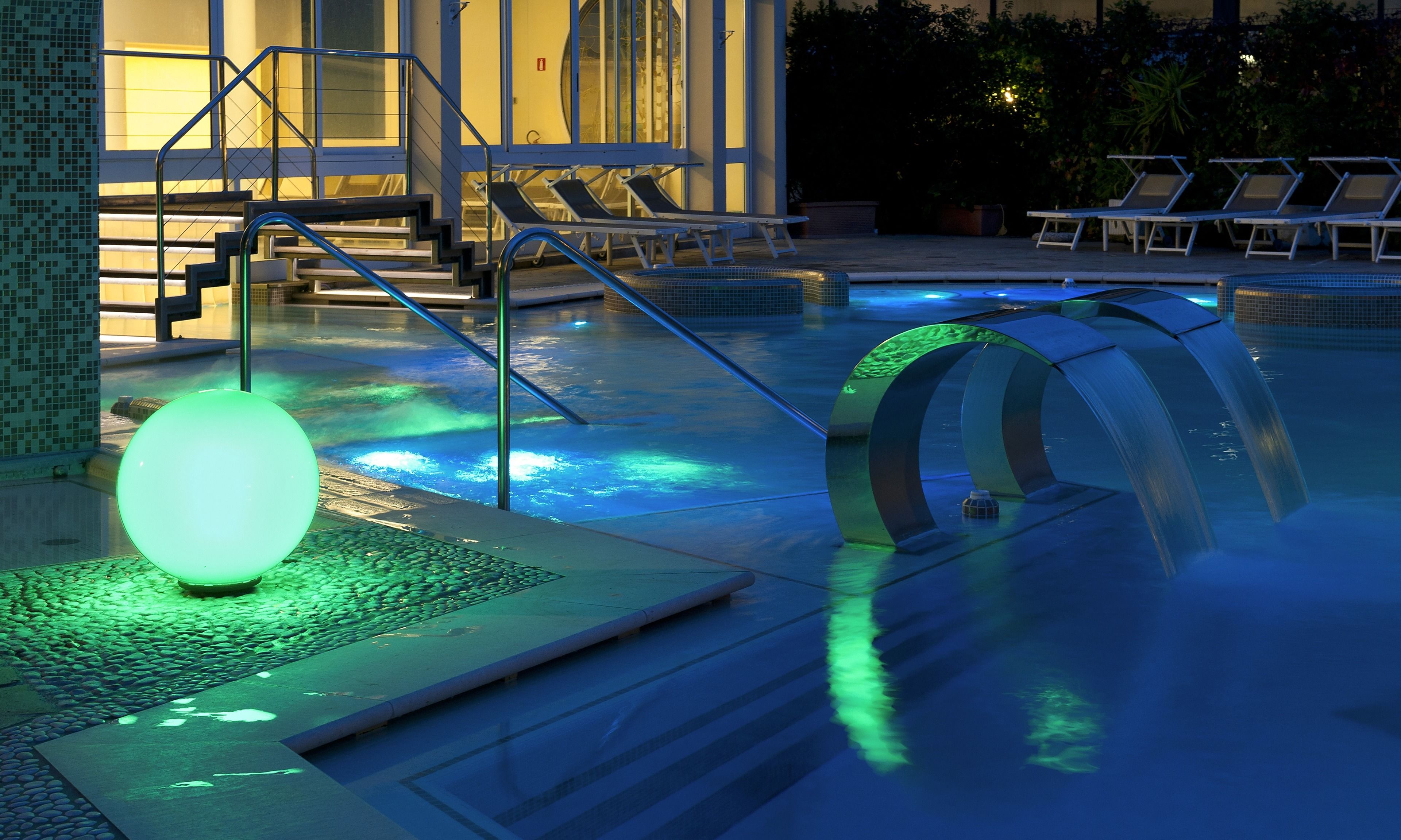 A swimming pool with a water feature, lounge chairs, and a staircase leading to a building.