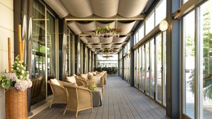 A covered outdoor seating area with wicker furniture and large windows. - Formentin Terme (Abano Terme)
