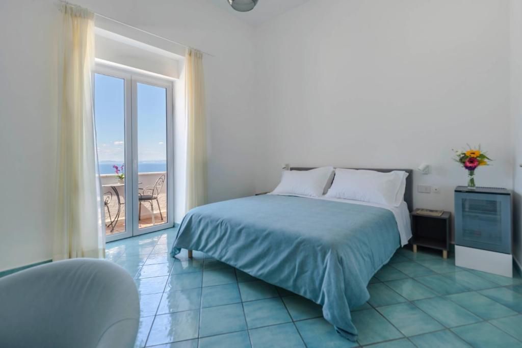Habitación de hotel con cama, mesita de noche, sillón y vistas a un espacio exterior a través de una puerta de vidrio.