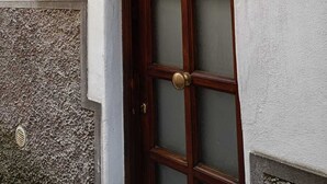 Een houten deur met ruitpanelen, een witte muur met een nummerplaatje, en een decoratief metalen element boven de deur.