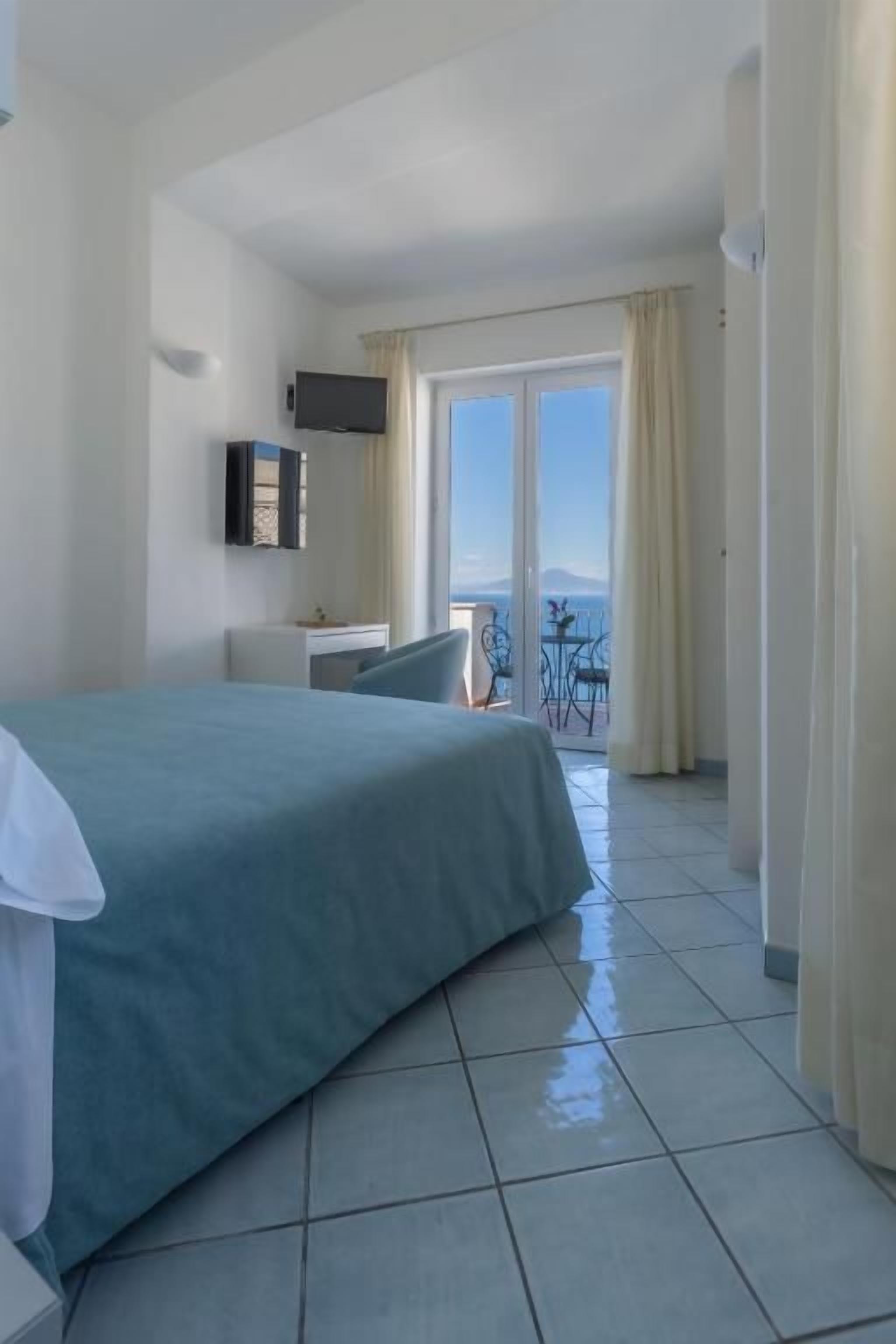 A hotel room with a bed, a desk, a chair, a TV, and a balcony with a view.