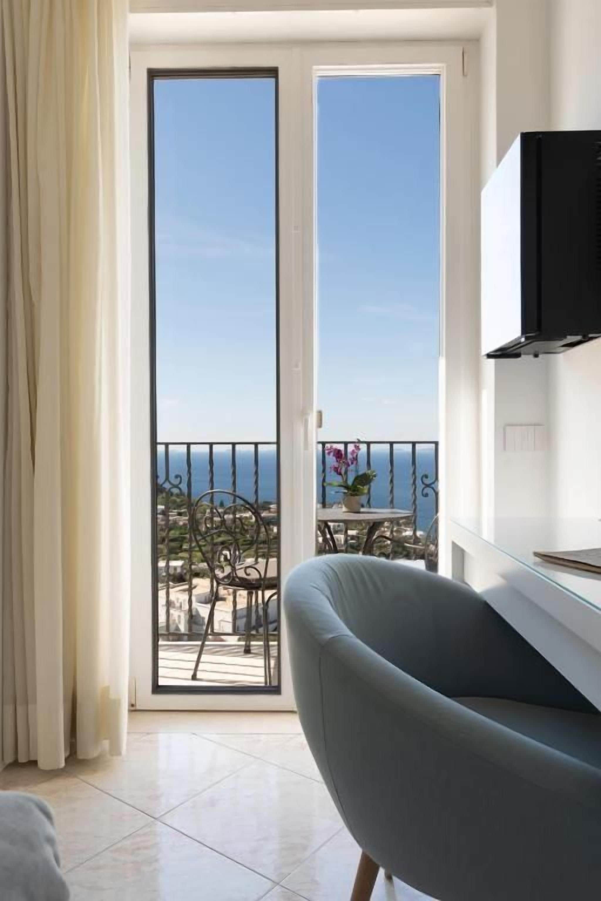 A room with a sliding glass door leading to a balcony with a view of the sea.