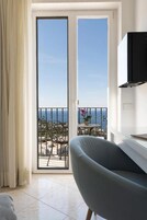 Una habitación con puerta corrediza de vidrio que da a un balcón con vista al mar.