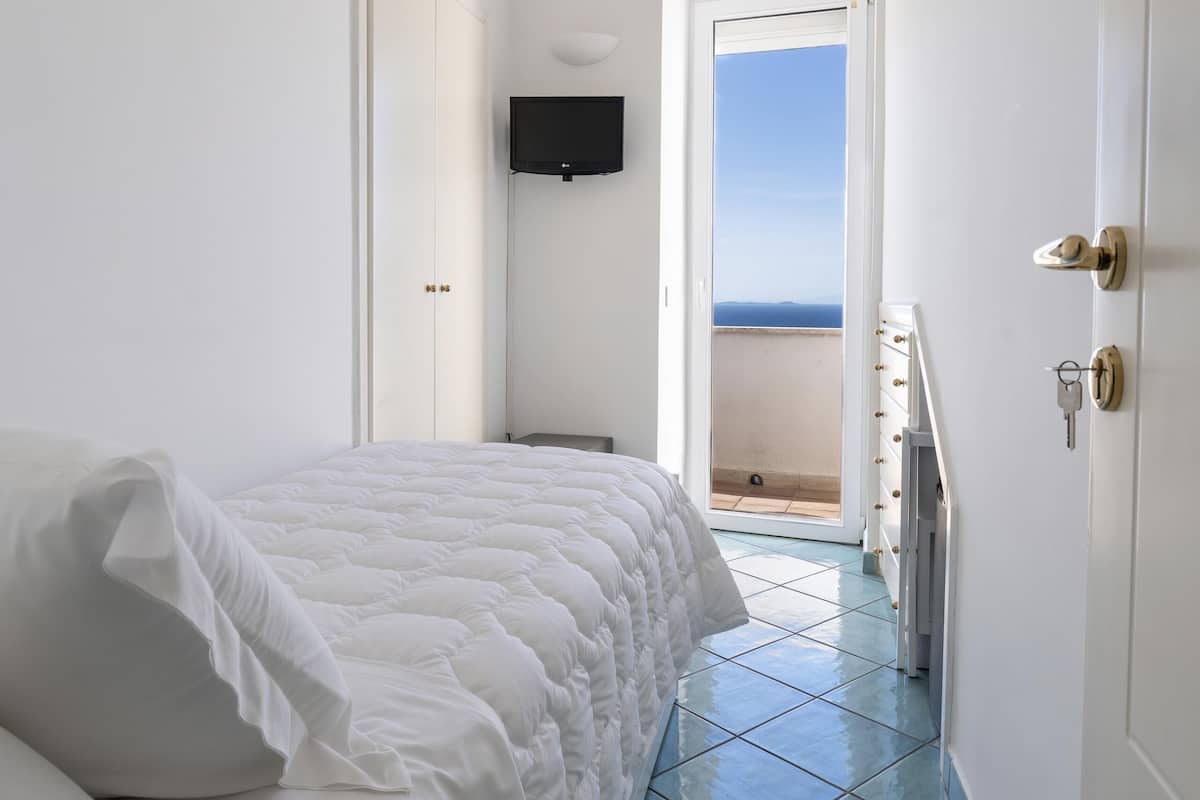 A bedroom with a bed, a television, and a door leading to a balcony with a view.