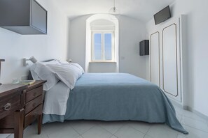 A bedroom with a bed, a dresser, a TV, and a window with a view of the sky. - Albergo La Prora (Capri)