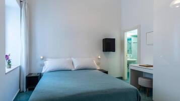 Een slaapkamer met een bed, nachtkastjes, een raam met gordijnen en een zichtbare badkamer door een open deur.