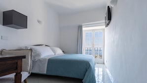 Een slaapkamer met een bed, een bureau en een stoel. Er is een raam met gordijnen en uitzicht op het omliggende landschap.