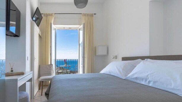 Een hotelkamer met een bed, een bureau, een stoel en een balkon met uitzicht op zee.