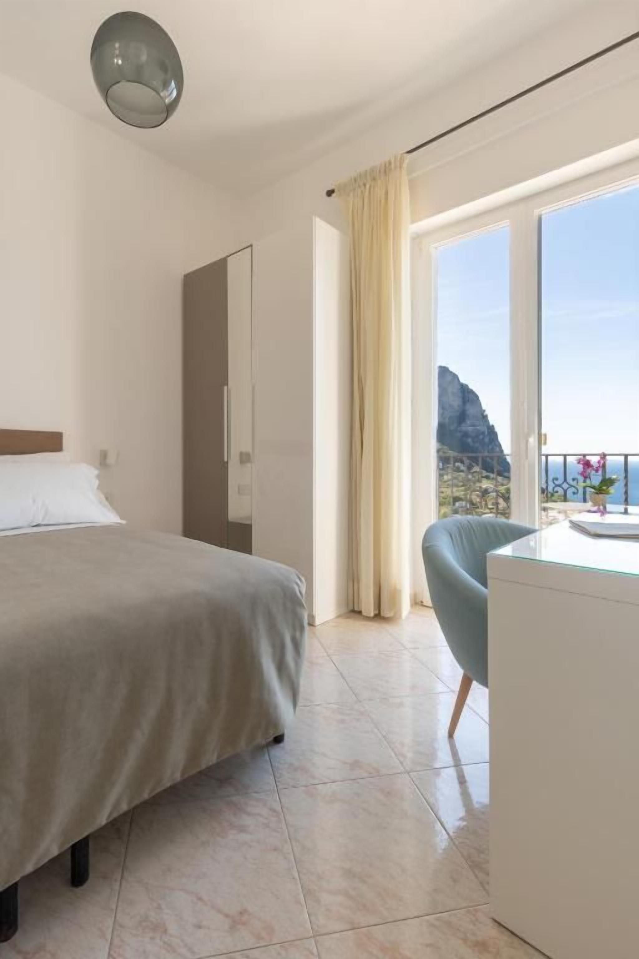 A hotel room with a bed, a desk, a chair, and a large window with curtains.