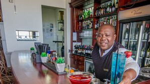 Un coin bar avec un barman, un cocktail rouge et une boisson bleue garnie d’une fraise.