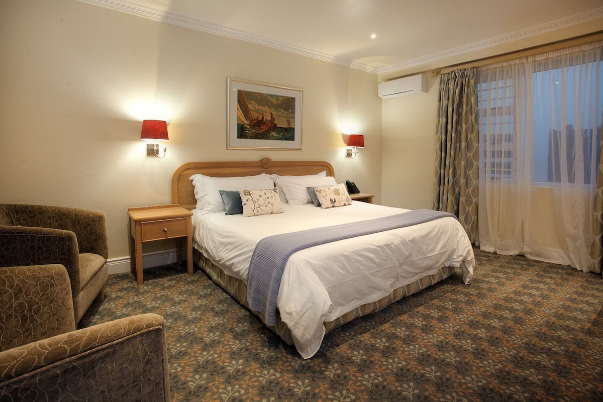 A hotel room with a large bed, two bedside lamps, a nightstand, a chair, and a window with curtains.