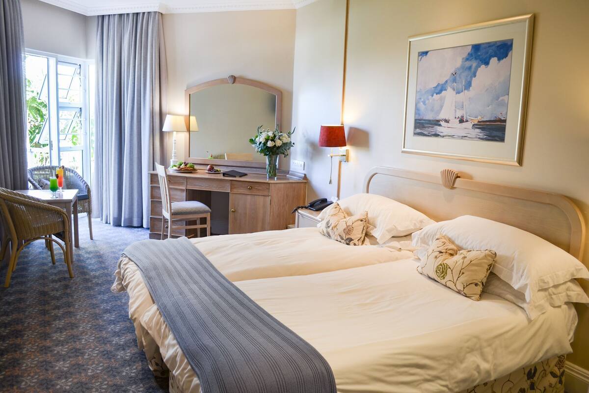 A hotel room with two beds, a desk, a chair, a lamp, and a painting on the wall.