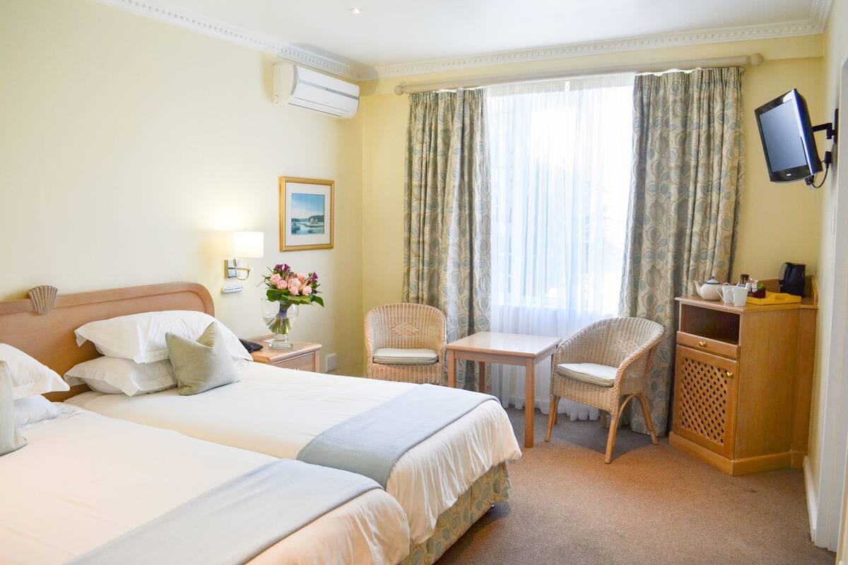 A hotel room with two beds, a desk, a chair, a TV, and a window with curtains.