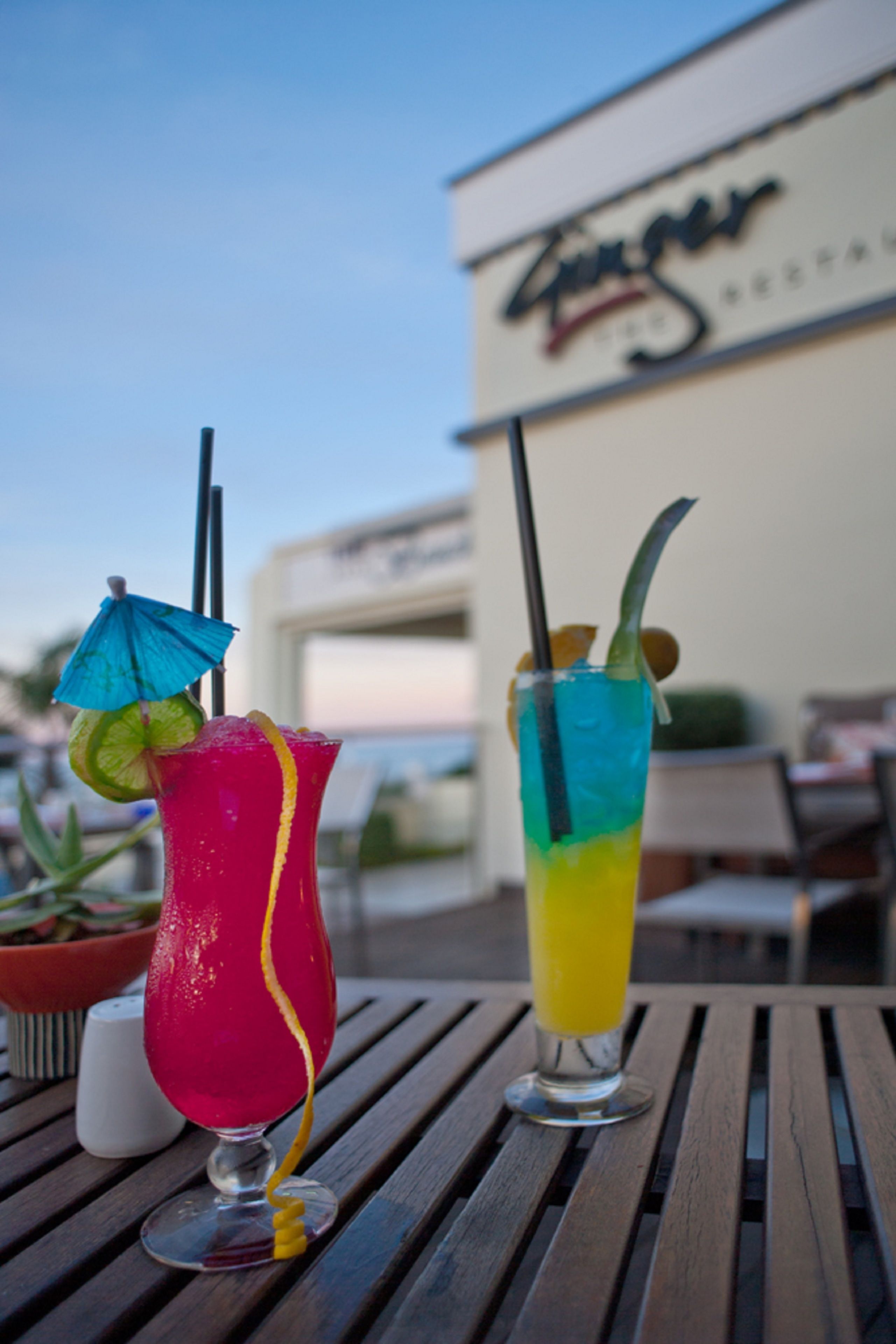 Two cocktails on a wooden table with a restaurant sign in the background.