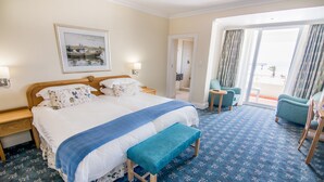 Une chambre d’hôtel avec un grand lit, un banc, une chaise et un balcon avec des rideaux.