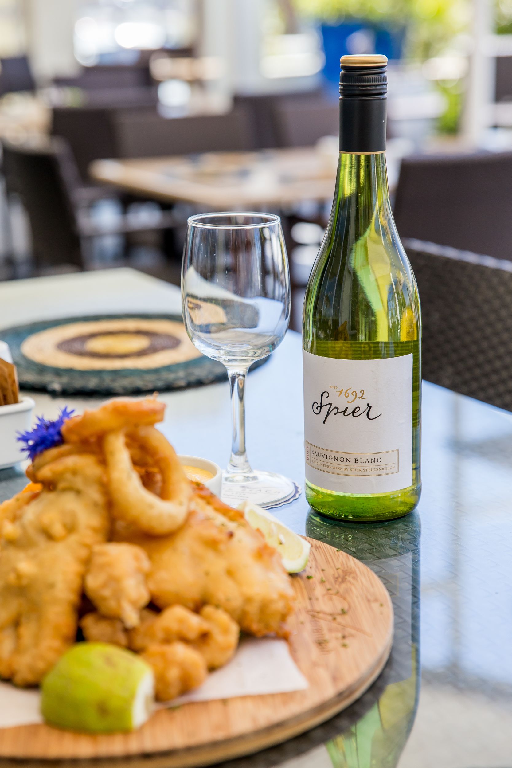 A bottle of 1692 Spier Sauvignon Blanc on a table with a plate of fried calamari and a glass of wine.