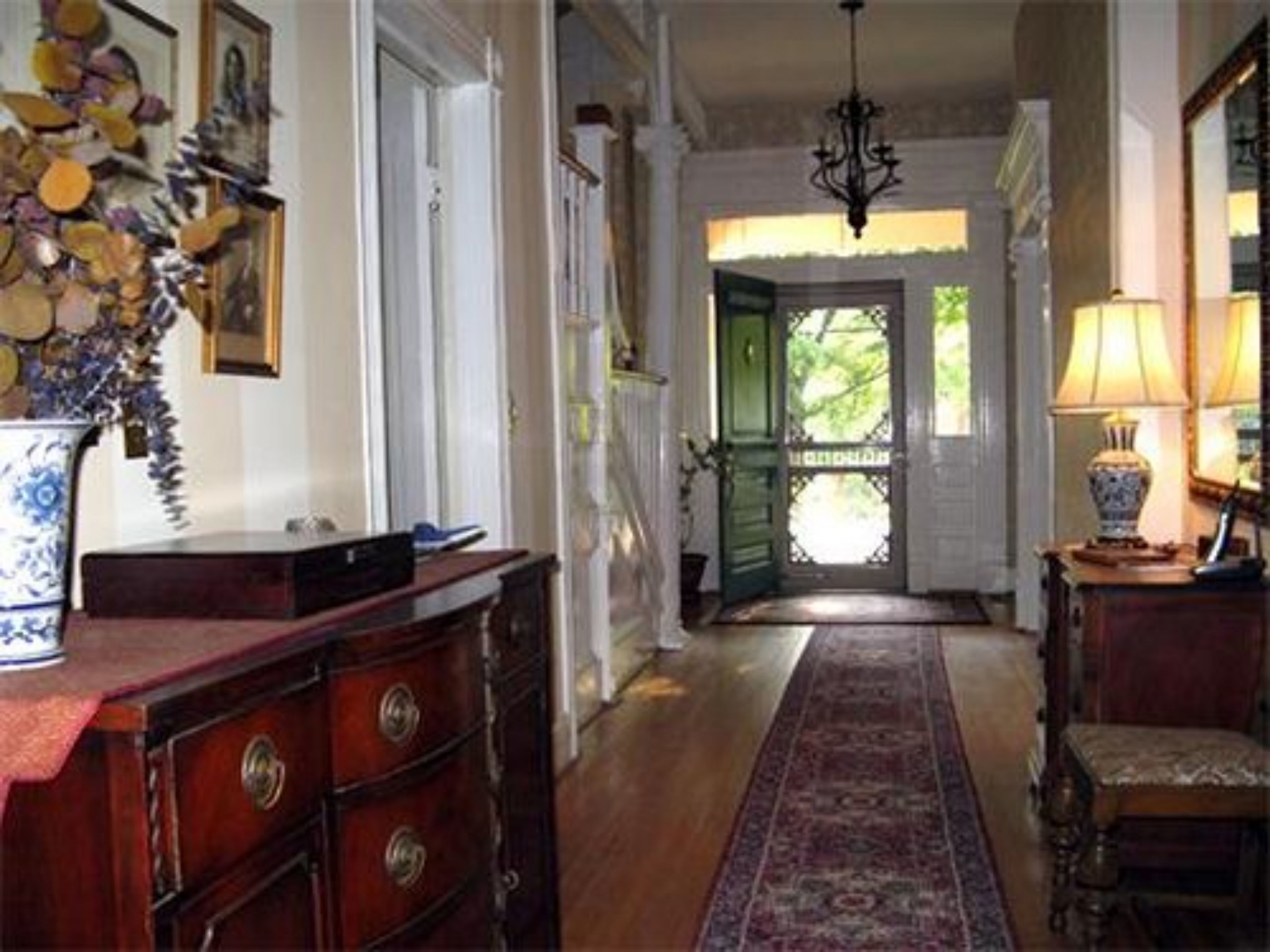 A hallway with a wooden dresser, a vase with flowers, a lamp, and a door leading to an outdoor area.