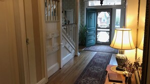 A hallway with a wooden floor, a patterned rug, a lamp, a vase with dried flowers, and a mirror. - Charles Bass House Bed & Breakfast (South Boston)