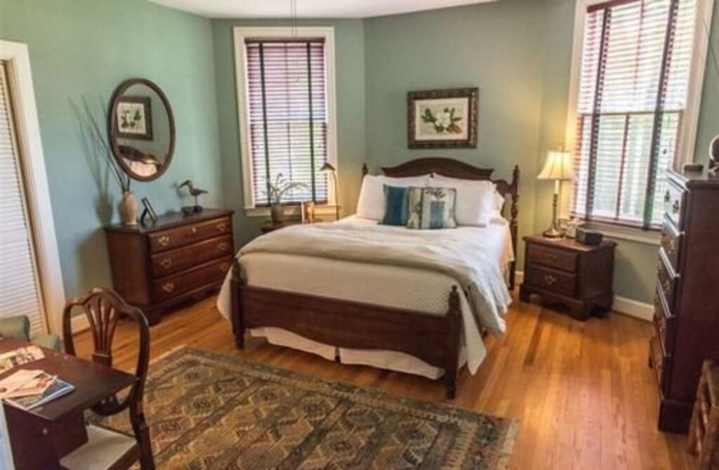 A bedroom with a large bed, two nightstands, a dresser, a chair, and a window with blinds.
