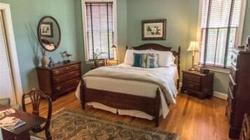 A bedroom with a large bed, two nightstands, a dresser, a chair, and a window with blinds.