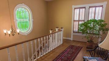 A staircase with a wooden handrail and white balusters, a red patterned rug, a potted plant, and a window with blinds.