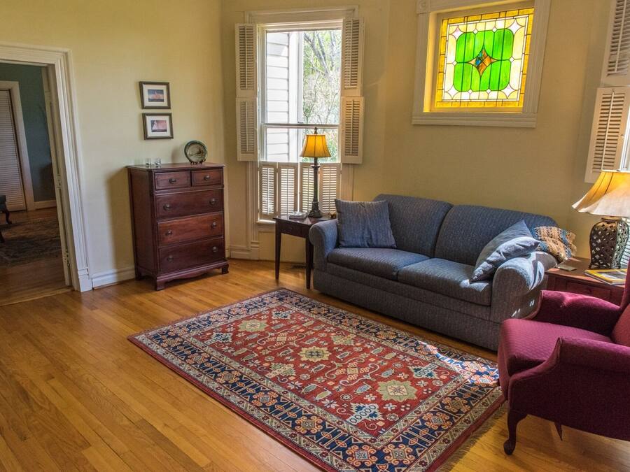 A living room with a wooden floor, a blue sofa, a red patterned rug, a wooden cabinet, and a stained glass window.
