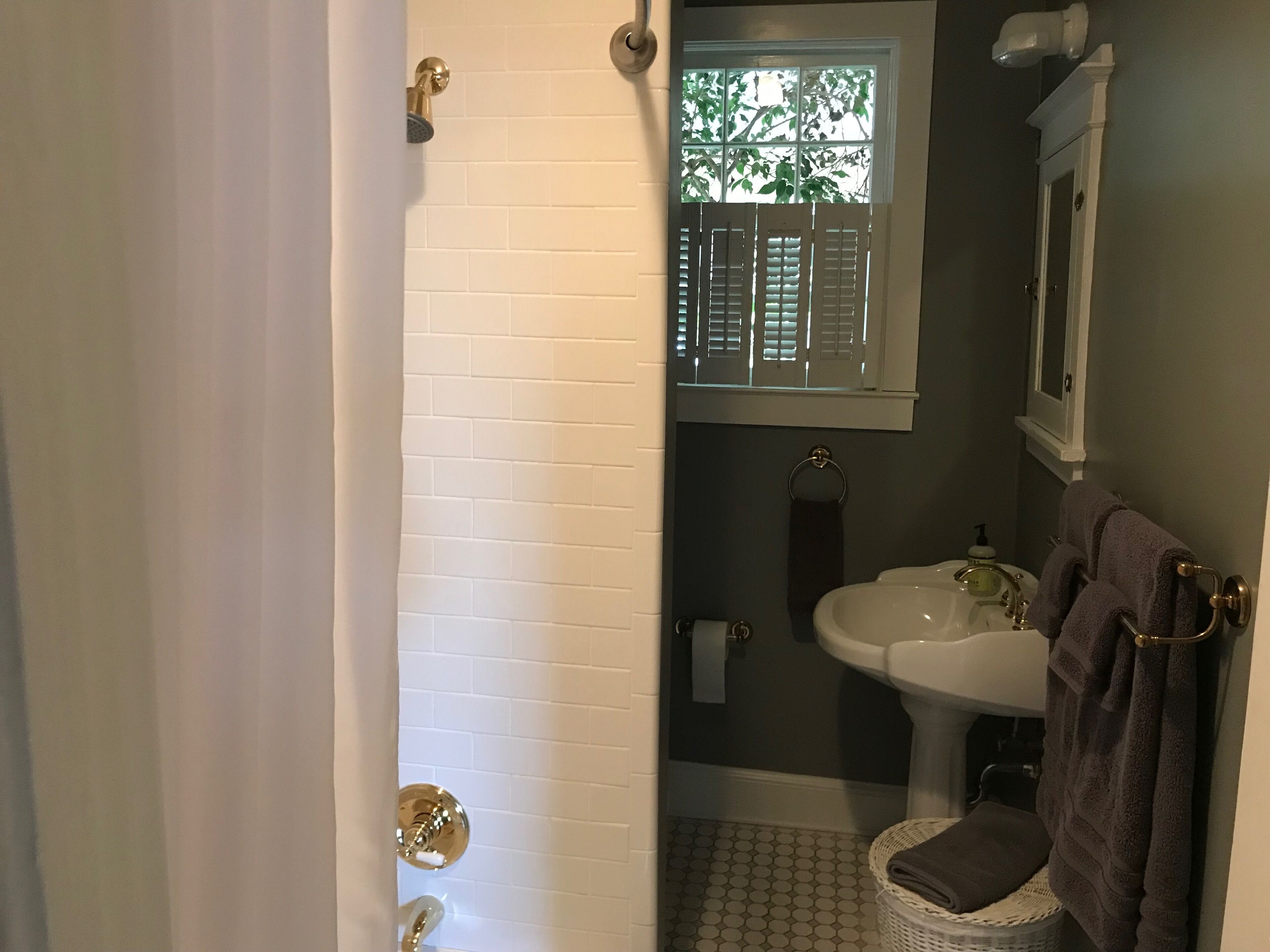 A bathroom with white tiled walls, a white sink, a window with shutters, and a towel rack.