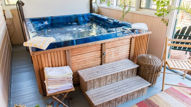 A hot tub with wooden steps and a bench, surrounded by windows and plants. - Charles Bass House Bed & Breakfast (South Boston)