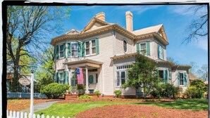 A two-story house with a front porch, a flag, and a white picket fence. - Charles Bass House Bed & Breakfast (South Boston)
