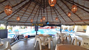 Zona de bar junto a la piscina con sillas y mesas de plástico blanco, techo de paja y lámparas de mimbre colgantes.