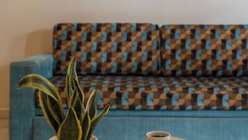Una sala de estar acogedora con un sofá estampado, una planta en maceta, una taza de café y un libro sobre una mesa.