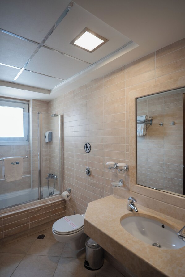 A modern bathroom with a glass shower enclosure, a sink with a mirror, and a toilet. - Molos Bay Hotel (Kissamos)