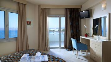 A hotel room with a bed, a desk, a chair, a TV, and a view of the sea.