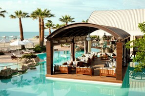 A pool area with lounge chairs and umbrellas, palm trees, and a view of the ocean. - Mediterranean Village Hotel & Spa (Katerini)