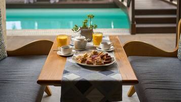 A poolside dining area with a table set for breakfast, overlooking a pool and lounge chairs.