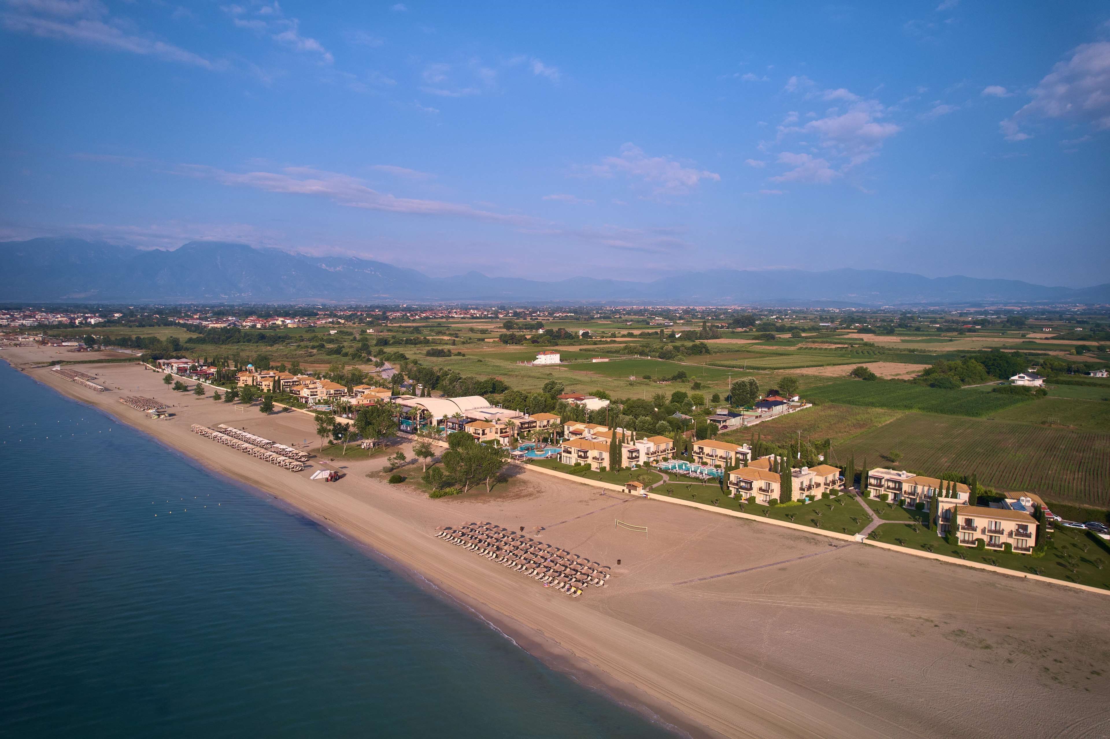Ein Luftbild eines Küstenresorts mit Strandvillen, einem Sandstrand und einem Bergpanorama im Hintergrund.