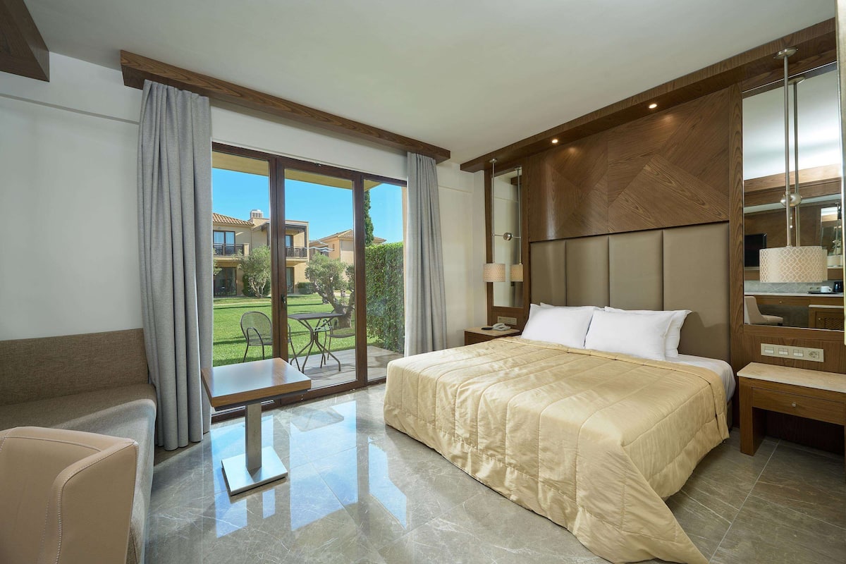 A hotel room with a large bed, a desk, a chair, and a view of the outdoors.
