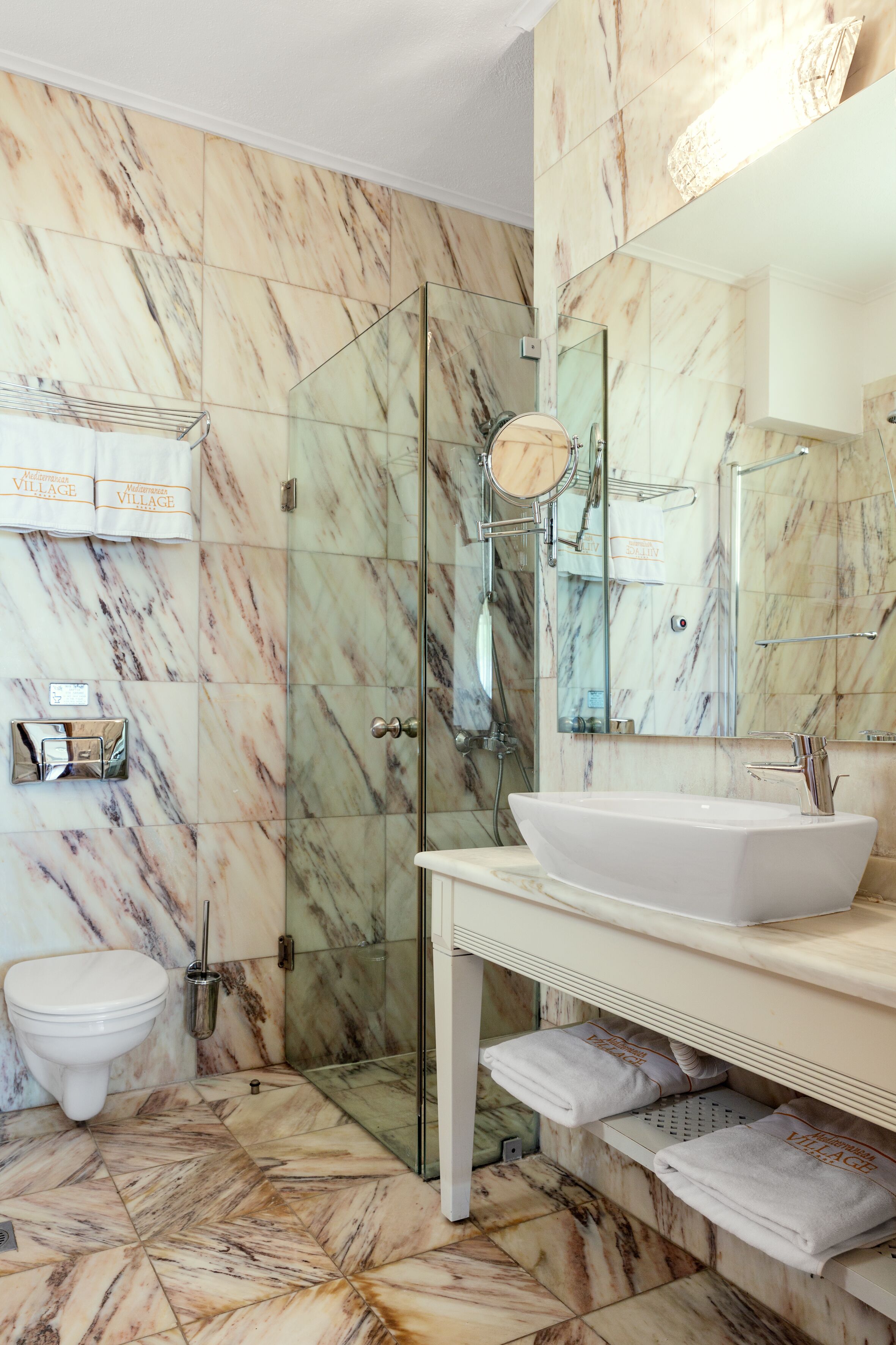 A bathroom with a marble floor, a glass shower enclosure, a white sink, and a toilet.