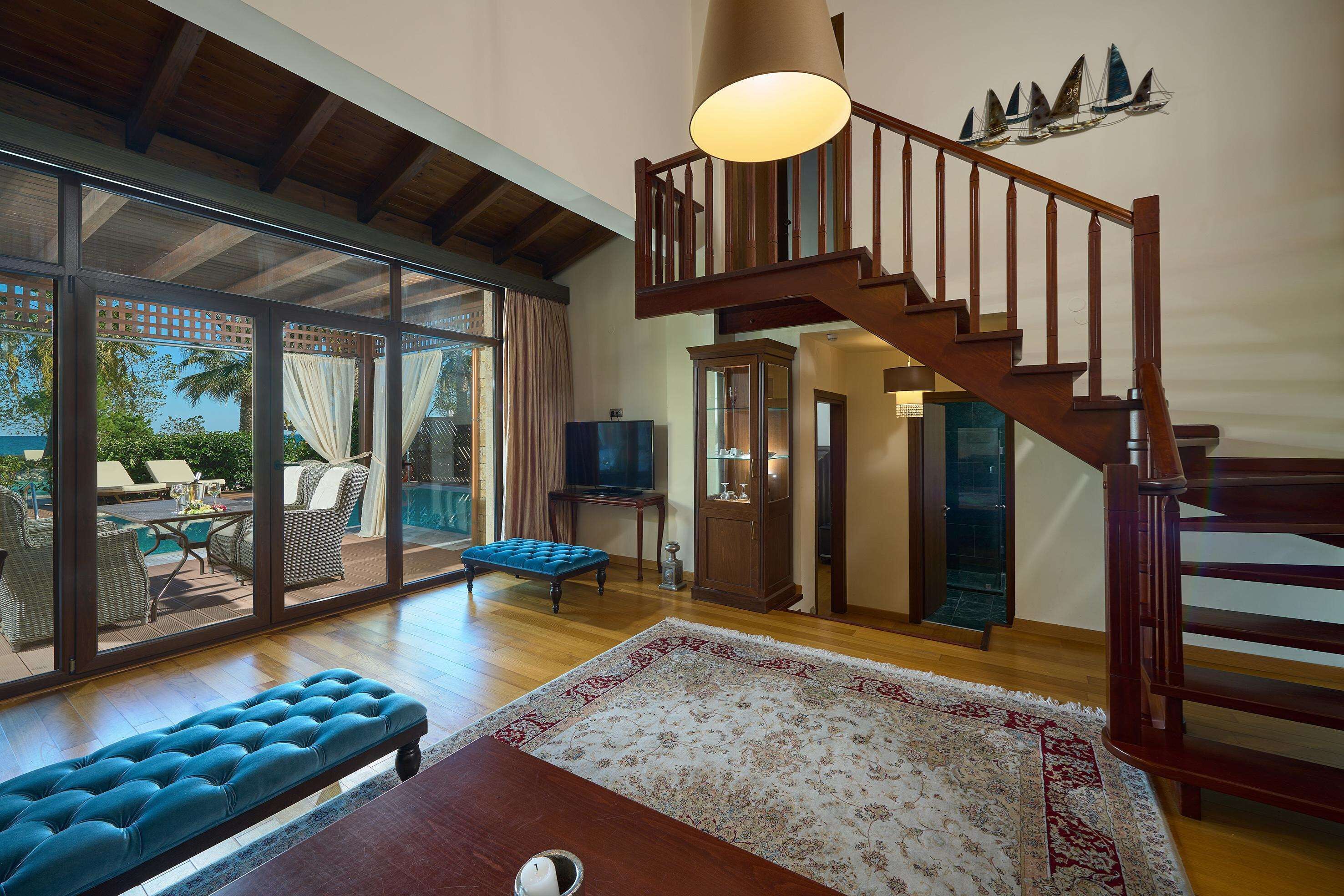 Un amplio salón con una escalera de madera, un ventanal con vistas a un patio y un banco azul.