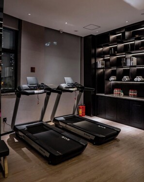A modern gym with treadmills, a fire extinguisher, and a wall-mounted shelf with bottles. - Paco Hotel Zhujiang New Town Saimachang Branch (Guangzhou)