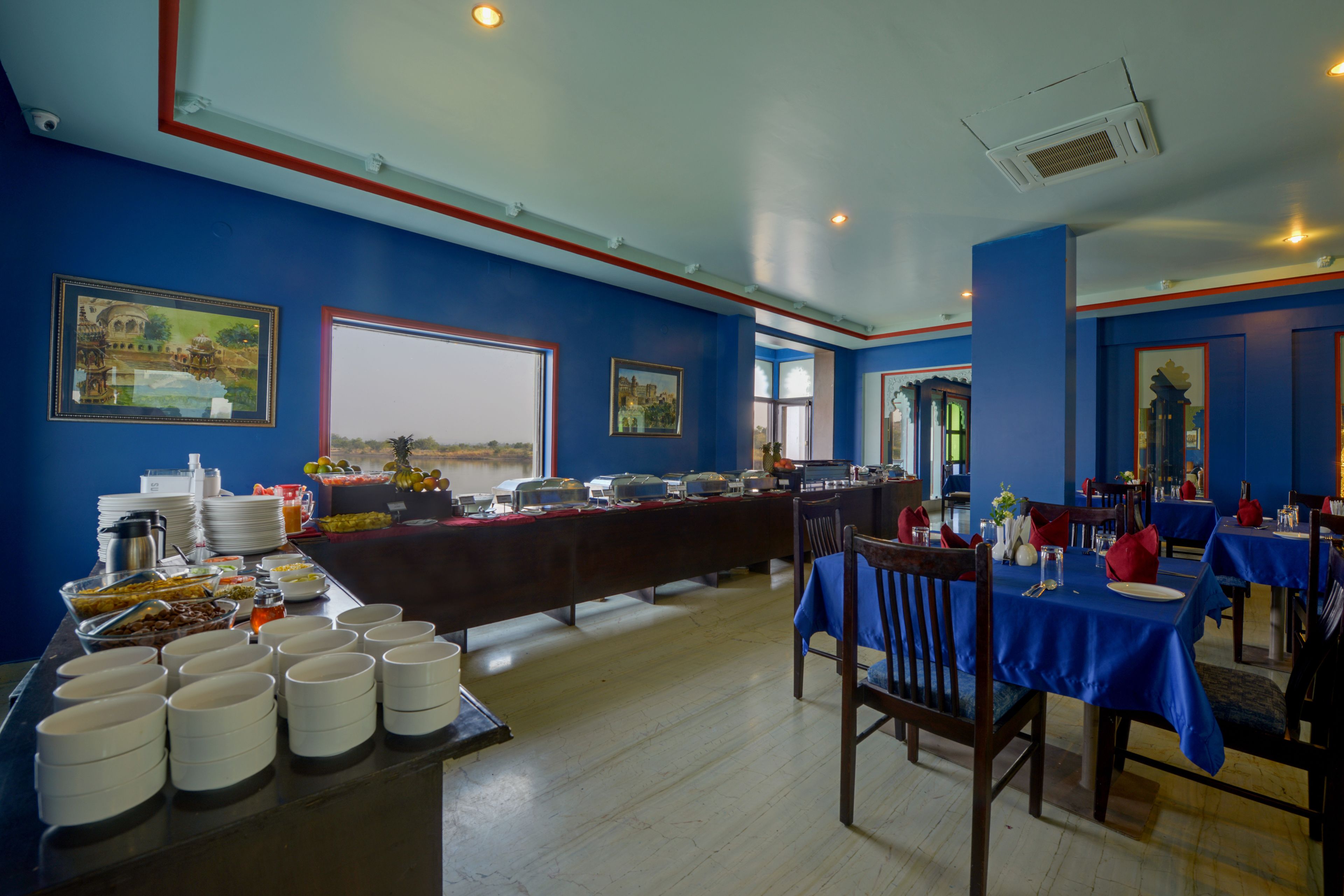 A dining area with blue walls, a buffet table with various food items, and multiple dining tables set with red napkins and white plates.
