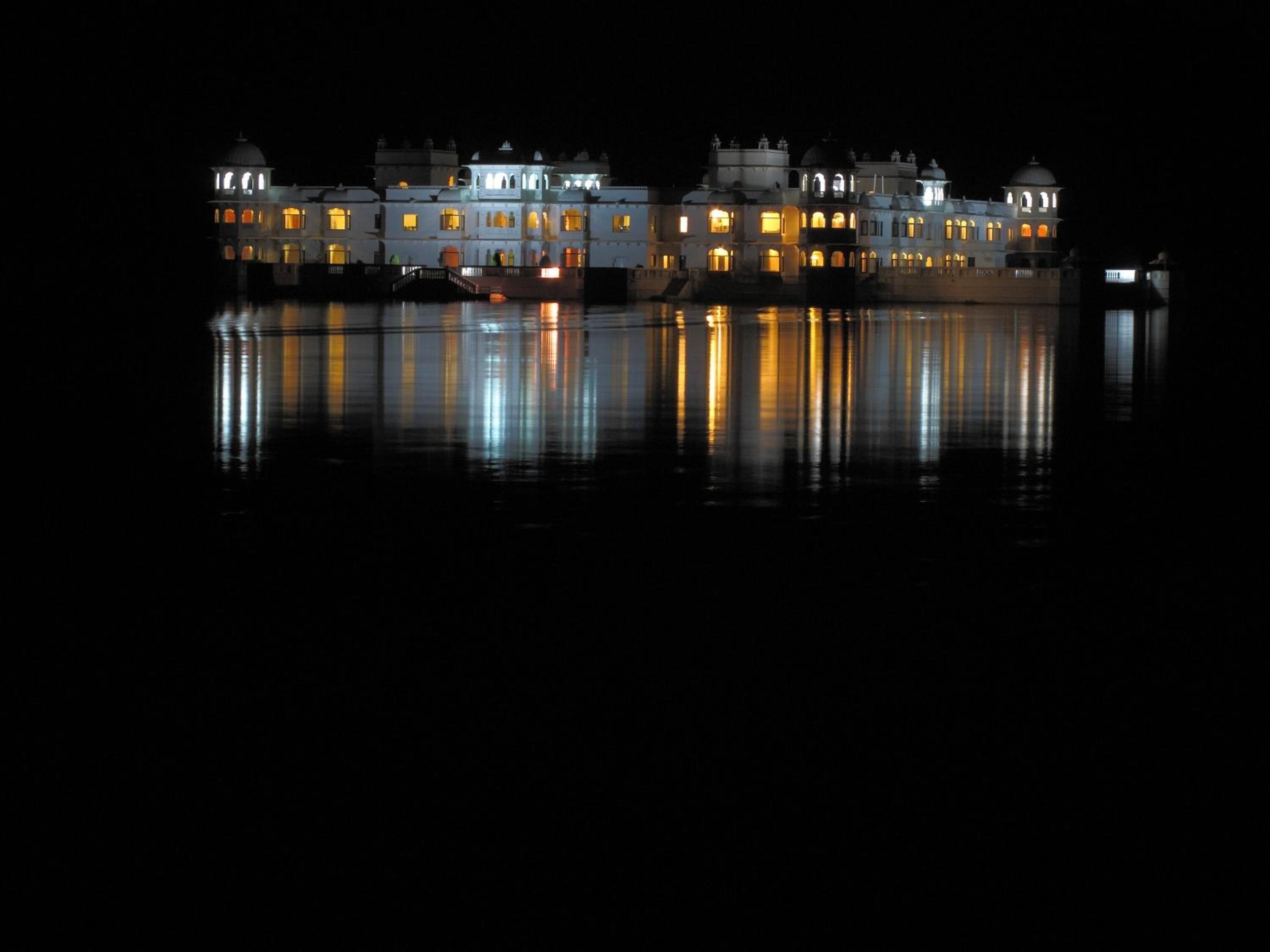 Un gran edificio iluminado con múltiples cúpulas y arcos, reflejado en el agua.